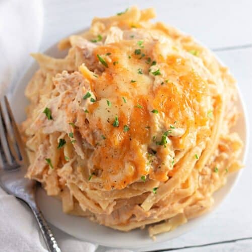 A plate of creamy pasta topped with melted cheese and chopped herbs, with a fork and a white napkin beside it.