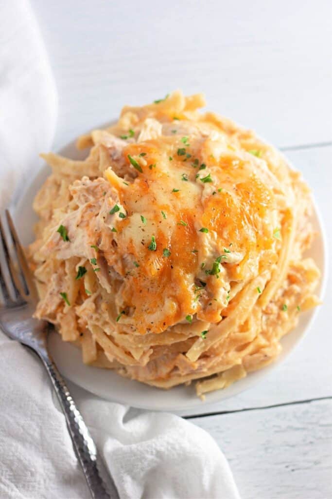 A plate of creamy pasta topped with melted cheese and chopped herbs, with a fork and a white napkin beside it.
