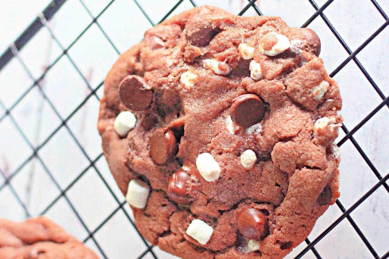 A close-up of a cocoa chip cookie with white and dark chocolate chunks resting on a black cooling rack.
