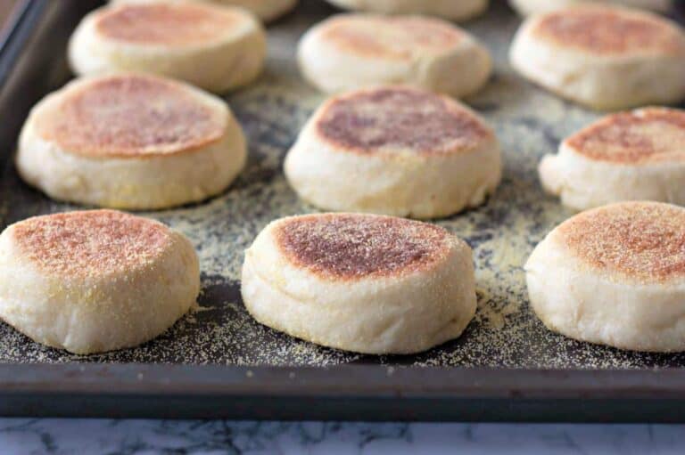 A baking tray with several English muffins, dusted with cornmeal