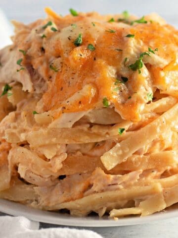 A plate of chicken tetrazzini topped with melted cheese and sprinkled with chopped herbs.