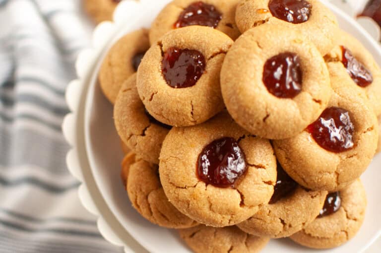 A plate of peanut butter cookies topped with red jelly, stacked neatly on a white cake stand.