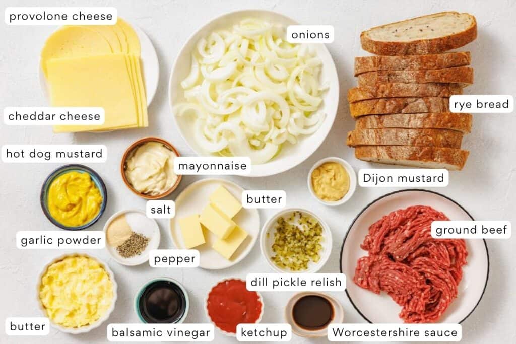 Various ingredients for making cheeseburgers are laid out, including ground beef, sliced bread, cheeses, condiments, seasonings, and sliced onions, all labeled for identification.