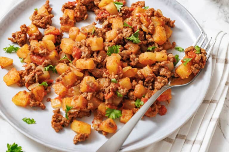 A plate of ground beef and diced potatoes cooked with tomatoes and garnished with herbs.