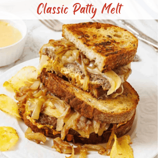 A classic patty melt sandwich with grilled onions and melted cheese on toasted bread, served with potato chips and a side of dipping sauce.