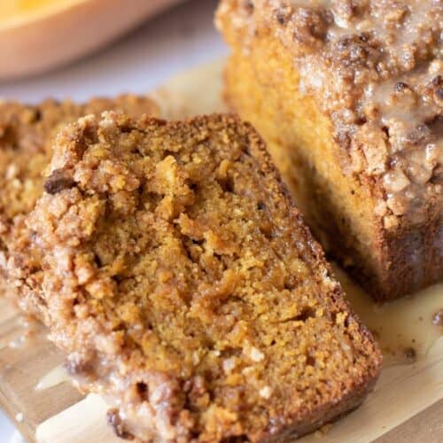 Close-up of sliced pumpkin bread with a crumbly, glazed topping on a wooden cutting board.