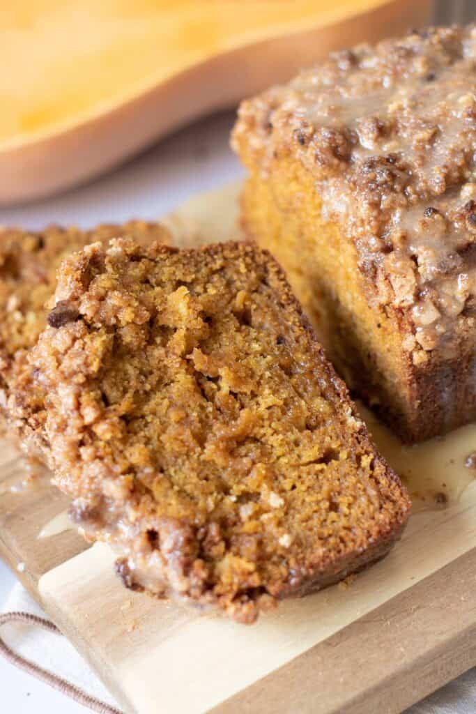 Close-up of sliced pumpkin bread with a crumbly, glazed topping on a wooden cutting board.