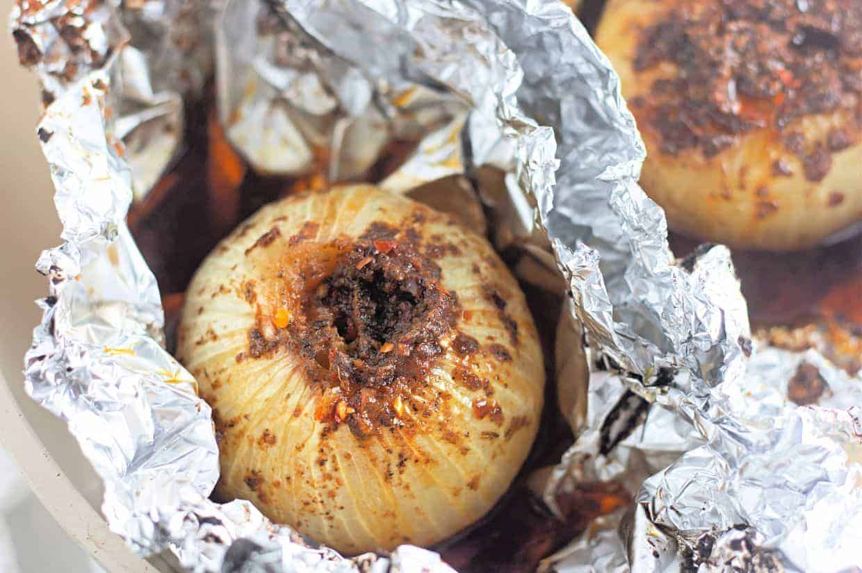 A whole onion stuffed with spices and seasonings, baked in foil with visible juices and browned bits.
