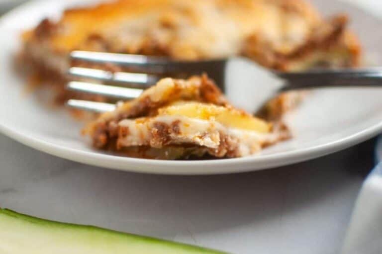 A close-up, slightly high-angle view of Zucchini Lasagna squares arranged on a dark gray baking sheet, each topped with a glossy, light brown apple filling and a generous sprinkle of light brown crumb topping.