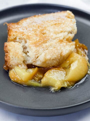 A serving of peach cobbler with a golden crust and peach filling on a black plate.