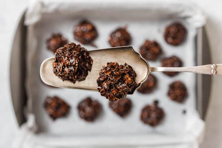 A metal spatula holds two chocolate oat cookies above a baking tray lined with parchment paper and filled with more cookies.