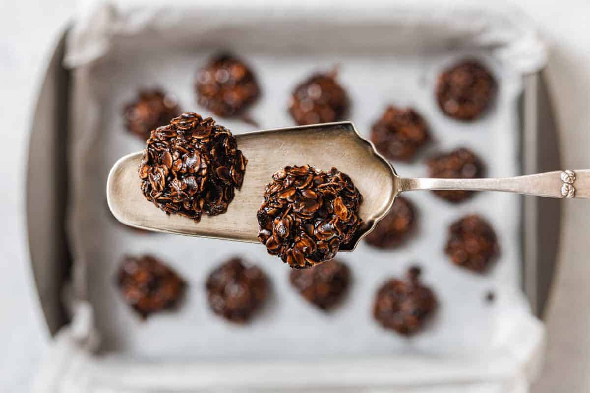 A metal spatula holds two chocolate Peanut Butter No-Bake Cookies above a baking tray lined with parchment paper and more cookies.