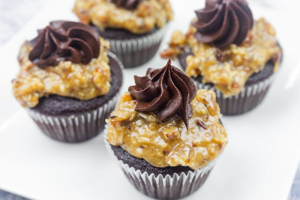 Chocolate cupcakes topped with a layer of coconut-pecan frosting and a swirl of chocolate frosting, arranged on a white plate.