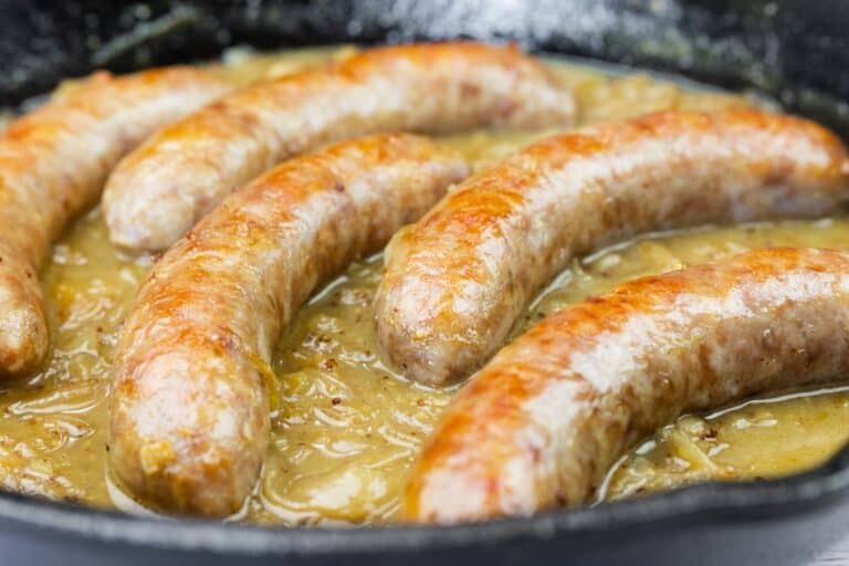Five beer-braised bratwurst cooking in a skillet with chicken broth and beer.