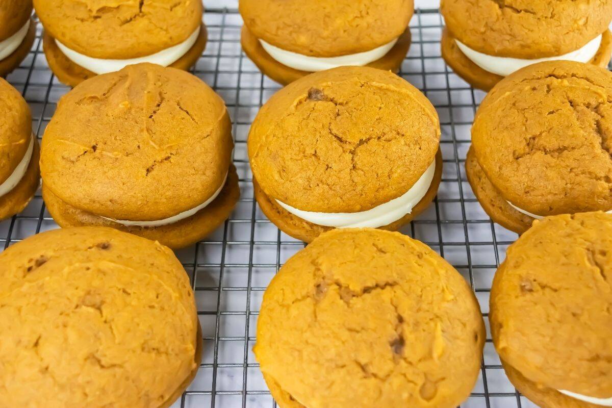 Pumpkin whoopie pies with cream filling are arranged in rows on a wire cooling rack.