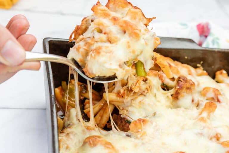 A hand lifts a serving of meatball casserole from a rectangular baking dish, showing melted cheese stretching.