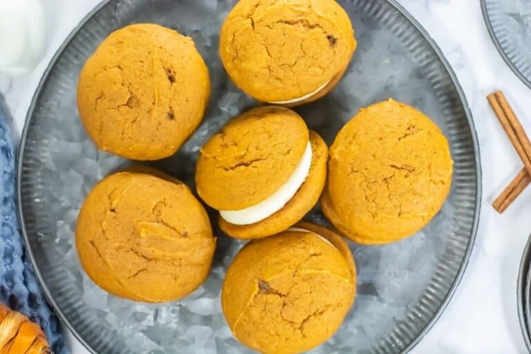 Six pumpkin whoopie pies with cream filling are arranged on a round gray plate, viewed from above.