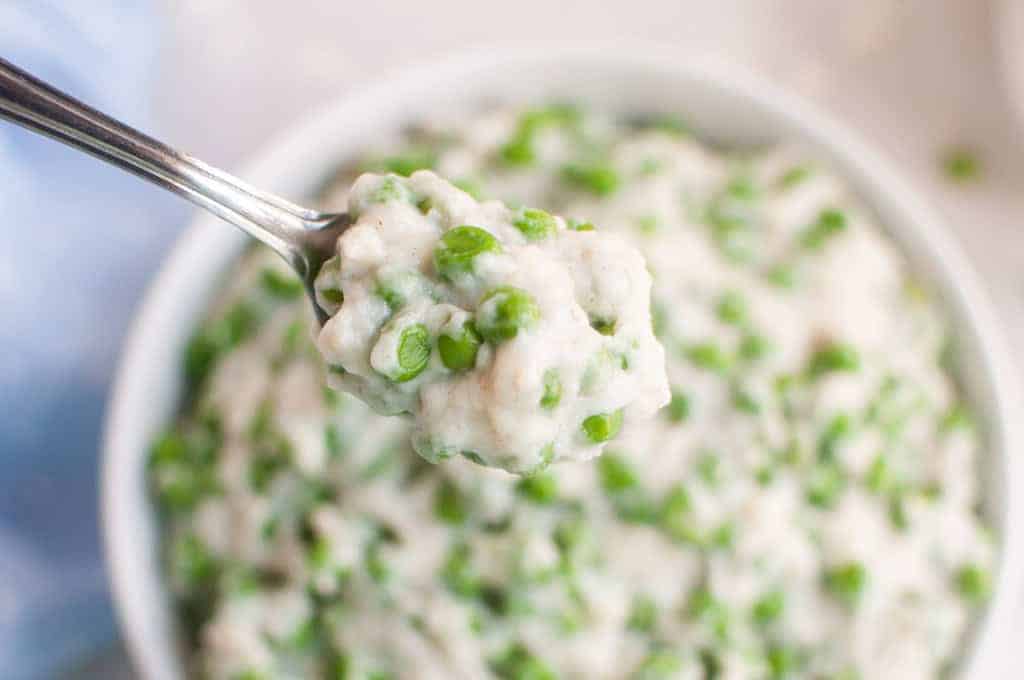 A spoonful of creamy peas held above a bowl filled with the same mixture.