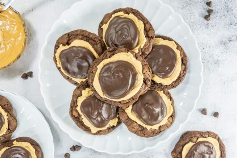 A white plate with several chocolate cookies topped with a layer of peanut butter and a layer of chocolate frosting, surrounded by scattered chocolate chips.