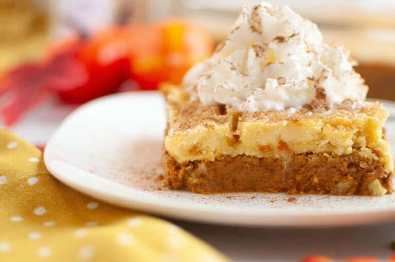 A slice of layered pumpkin dessert topped with whipped cream and sprinkled with cinnamon, served on a white plate.