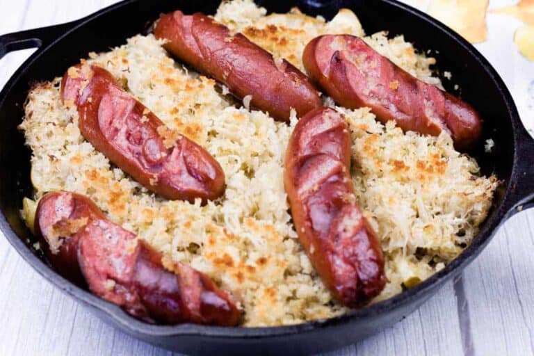 A cast iron skillet filled with sliced sausages on top of a bed of sauerkraut and baked breadcrumbs.