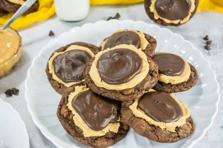 A plate of chocolate cookies topped with a layer of peanut butter and a layer of chocolate frosting, placed on a white plate.