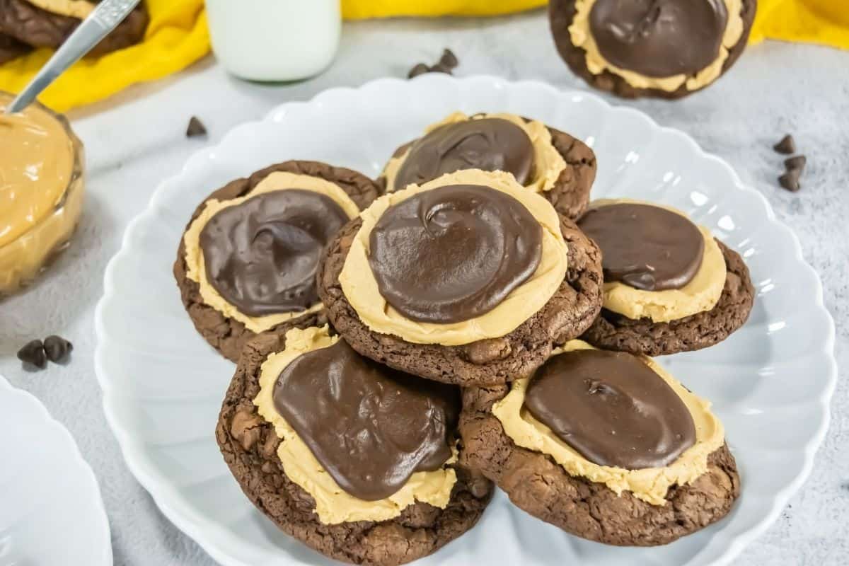 A white plate holds several chocolate cookies topped with a layer of peanut butter and a swirl of chocolate frosting.