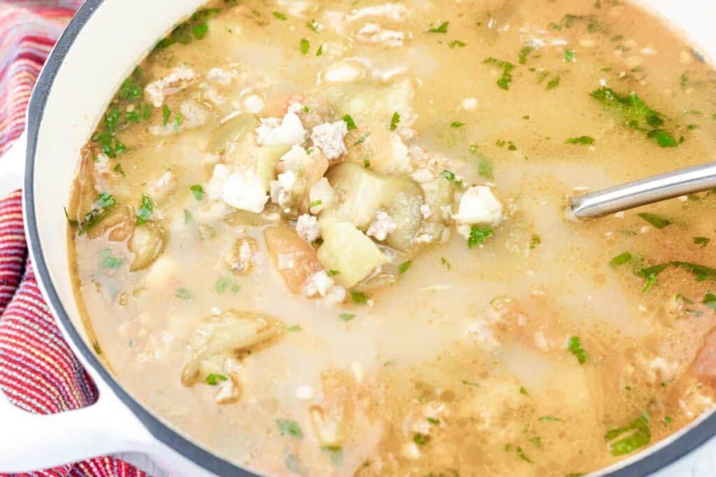 A pot of Green pork posole soup with ground meat, vegetables, herbs, and broth, with a metal ladle resting inside.