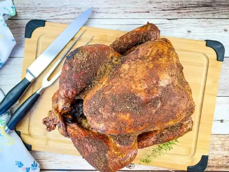 A whole roasted turkey on a wooden cutting board with a carving knife and fork beside it.