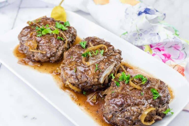 Three Salisbury steak patties topped with onions and gravy, garnished with parsley, served on a white rectangular plate.