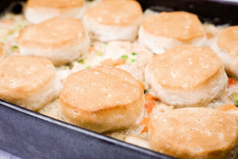 A baking dish filled with creamy chicken and vegetable filling topped with golden-brown biscuits.