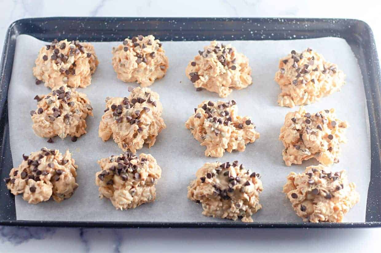 A baking tray lined with parchment paper holds twelve Avalanche Crunch Cookies.