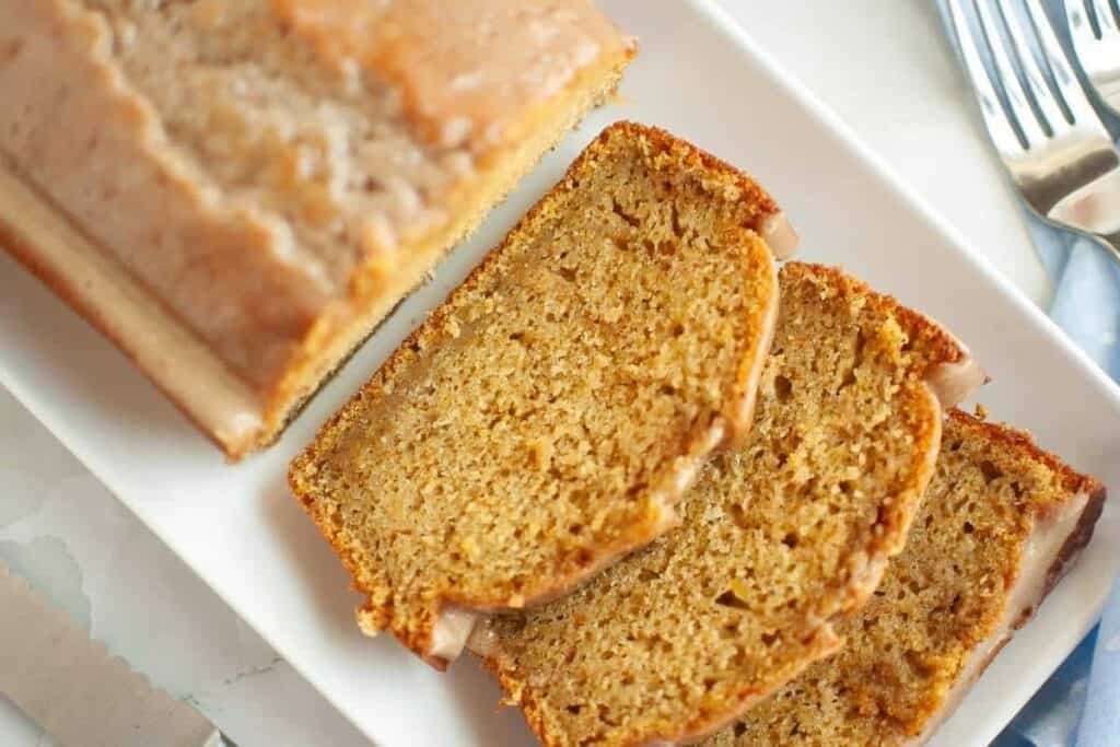 Sliced loaf of glazed bread on a white rectangular plate with three pieces cut and arranged in front.