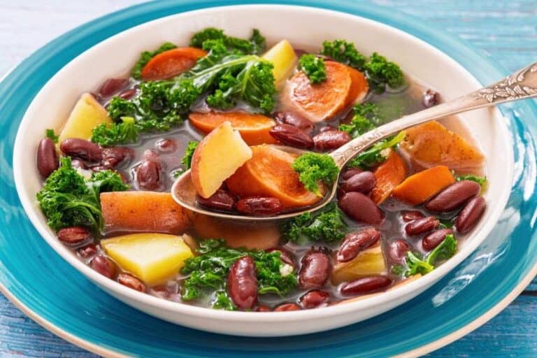 A bowl of Sausage & Kale Soup, served with a spoon on a blue-rimmed plate.
