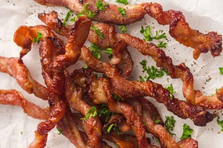 Crispy, twisted strips of cooked bacon garnished with chopped parsley on a sheet of parchment paper.