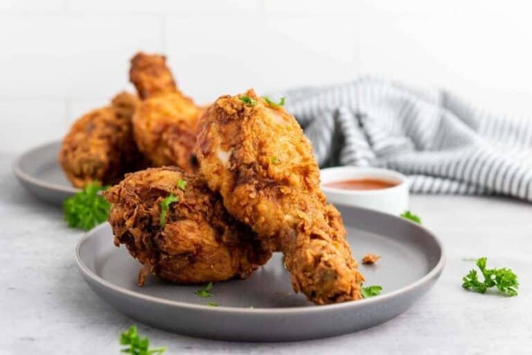 Two plates with crispy fried chicken drumsticks garnished with parsley, served with a small bowl of dipping sauce and a striped kitchen towel in the background.