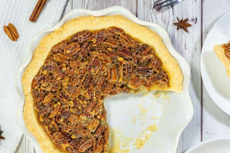 A pecan pie with a large slice missing, shown in a white pie dish on a wooden surface.