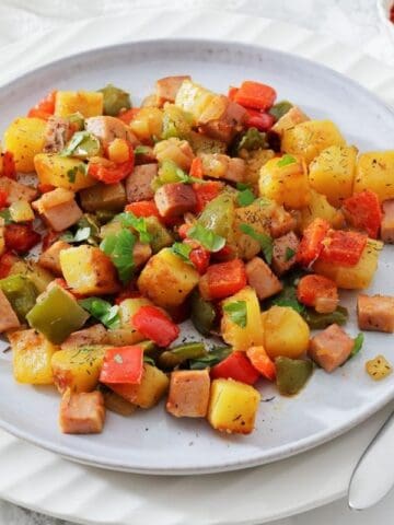 A plate of Denver Breakfast Potatoes garnished with herbs, with a fork and a dish of paprika on the side.