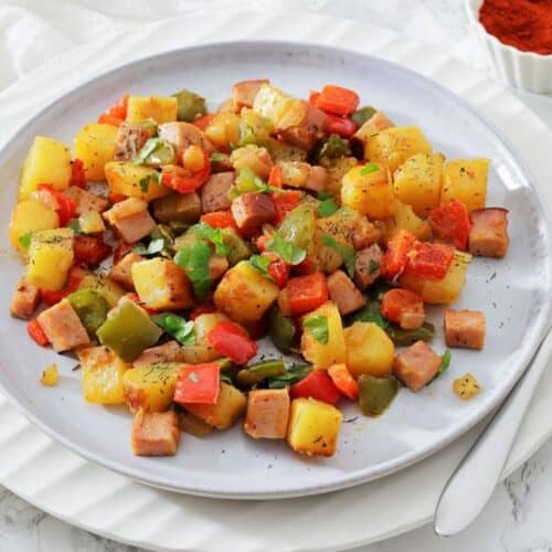 A plate of Denver breakfast potatoes garnished with herbs, with a fork and a dish of paprika on the side.