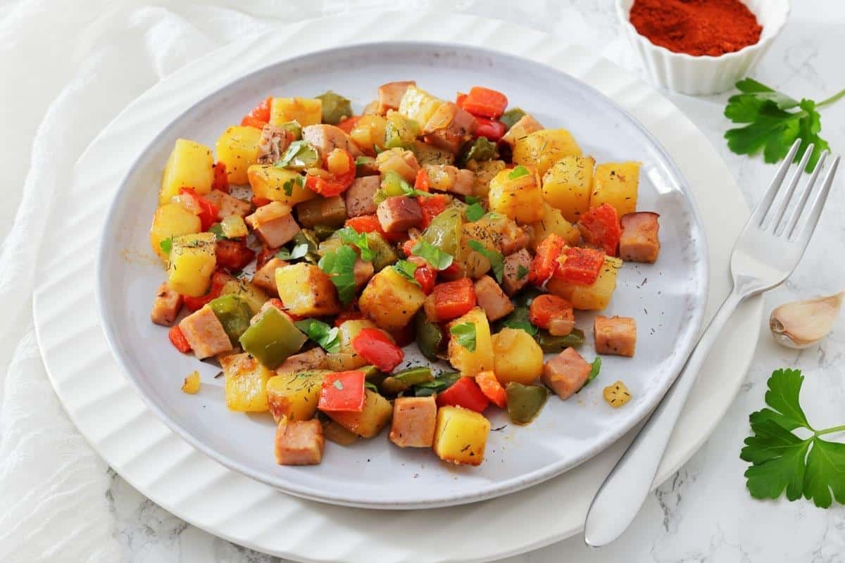 A plate of Denver Breakfast Potatoes garnished with herbs, with a fork and a dish of paprika on the side.