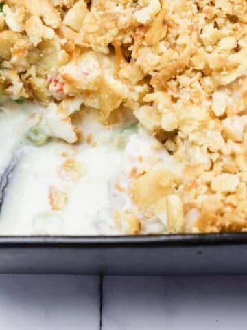 A partially served casserole dish with a creamy filling, topped with a golden crumb crust, shown in a black baking pan.