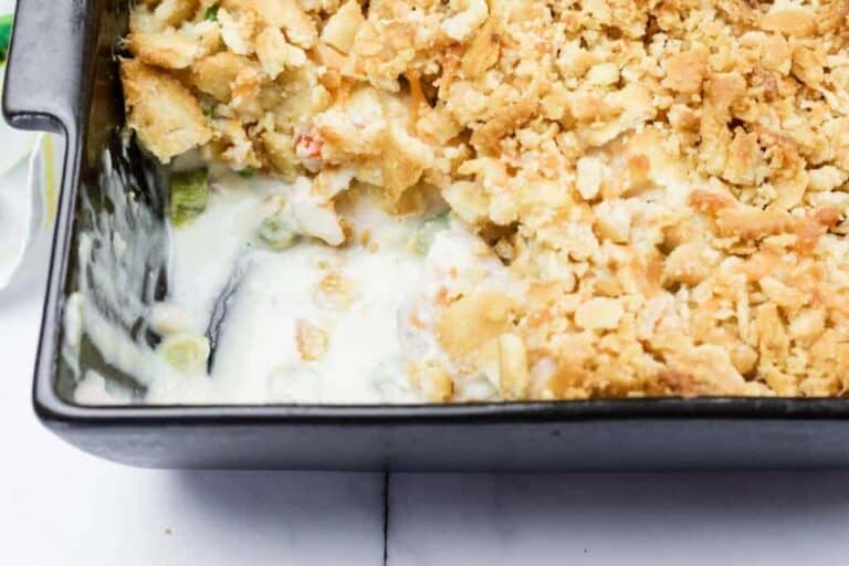 A partially served casserole dish with a creamy filling, topped with a golden crumb crust, shown in a black baking pan.