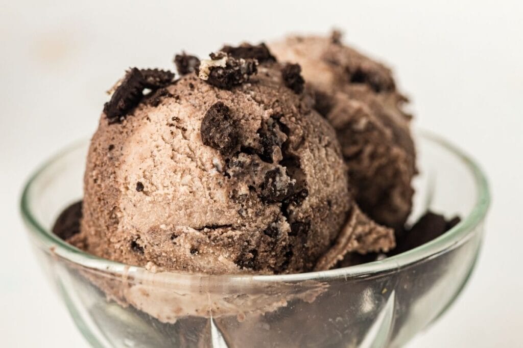 Two scoops of chocolate ice cream with cookie pieces served in a clear glass bowl.