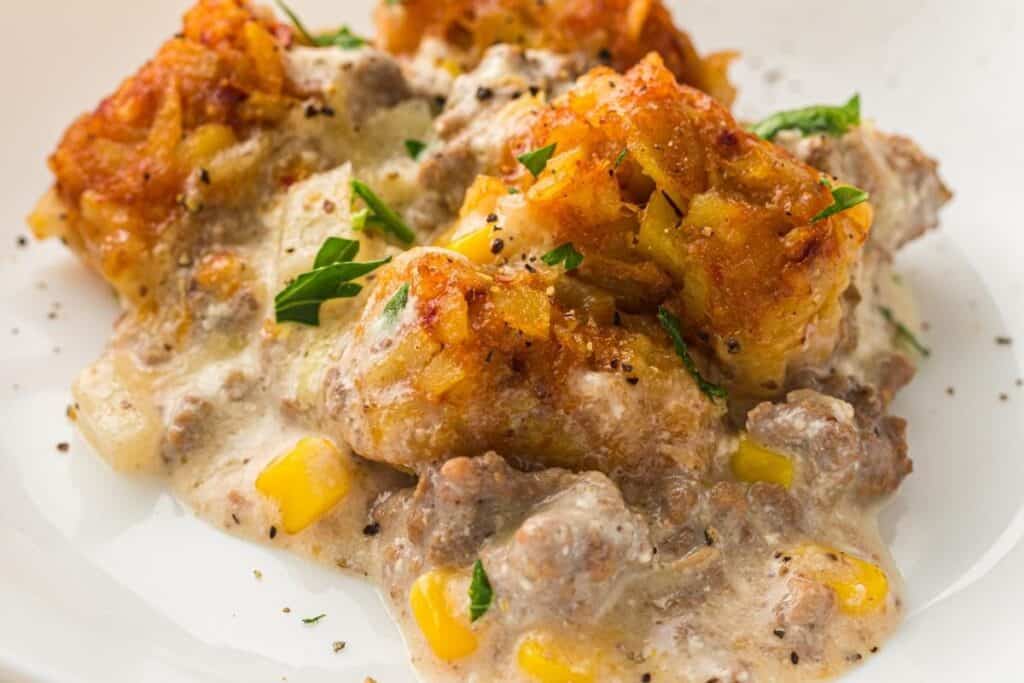 A serving of Slow Cooker Cowboy Casserole topped with crispy tater tots and black pepper on a white plate.
