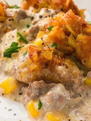A serving of Slow Cooker Cowboy Casserole topped with crispy tater tots and black pepper on a white plate.