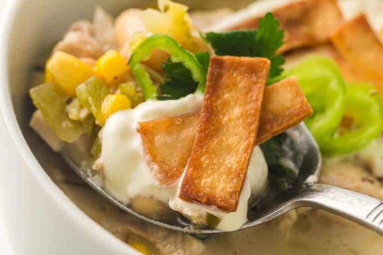 A close-up of a spoonful of white chili topped with sour cream, crispy tortilla strips, corn, jalapeño slices, and cilantro.