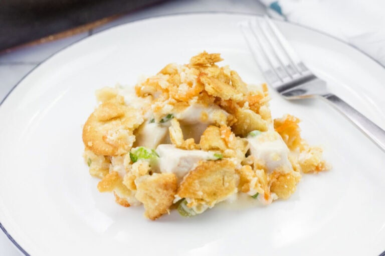 A serving of creamy chicken casserole topped with crispy crackers on a white plate with a fork.