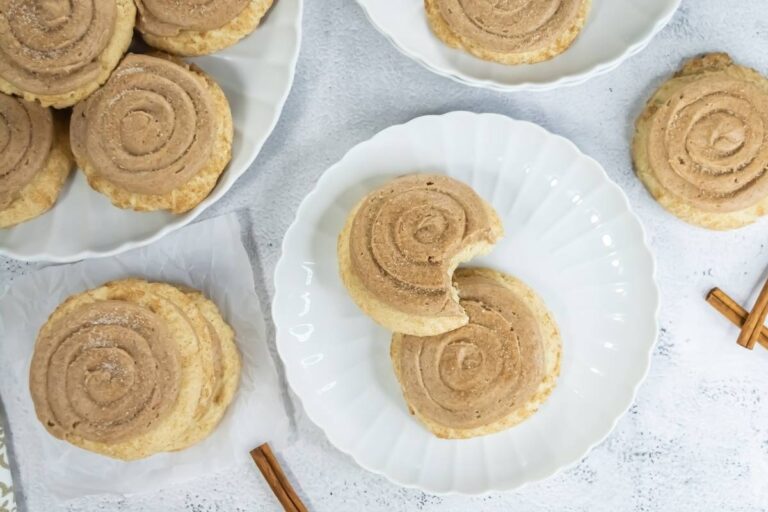 Several round cinnamon sugar cookies are displayed on white plates, with one cookie on a plate showing a bite taken out. Cinnamon sticks are placed nearby.