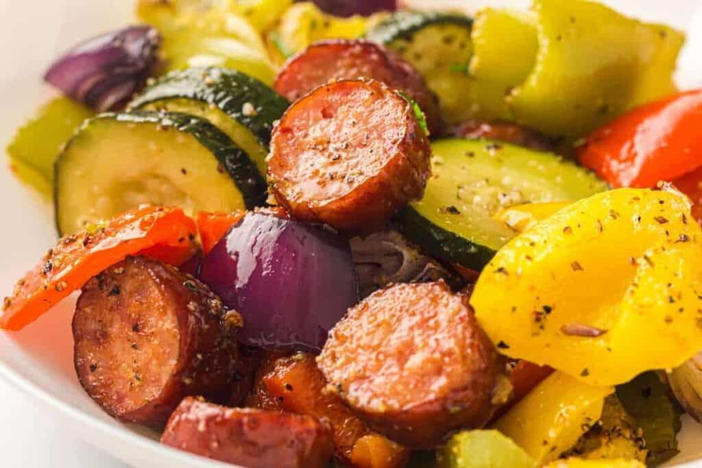 Sliced sausage, zucchini, red onion, and bell peppers seasoned with herbs and spices on a white plate.