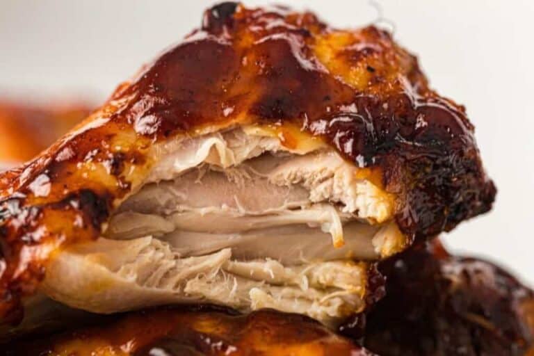 Close-up of a cooked chicken wing with barbecue sauce, showing a bite taken out to reveal the juicy, tender meat inside.